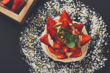 Bir tatlı siyah bir masanın üzerine konur. Taze çilek ve fındık ile süslenmiş. Yanında fazladan çilek içeren ahşap bir tabak var. Sahne öğleden sonra bir kafede geçiyor..