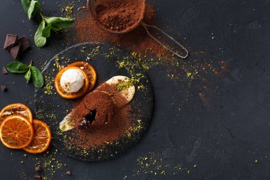 Bir tatlı siyah bir tabakta düzenlenir. Sergide çikolata, dondurma, portakal dilimleri ve nane yaprakları yer alıyor. Kakao tozu tabağın etrafına serpilmiş, doku ve lezzet katıyor..