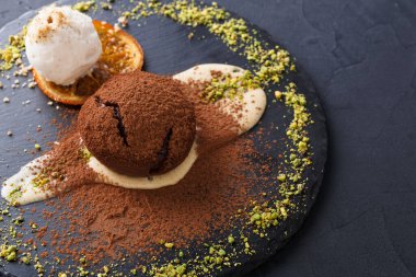 Çikolatalı bir tatlı siyah bir tabağa konur. Tatlı kremayla kaplı ve yanında da bir portakal dilimi var. Fındık ezmesi ve kakao tozu Tatlının etrafını sarmış.