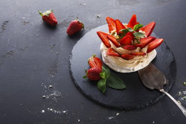 Koyu bir tahta yüzeyde bir tatlı düzenlenir. Sergide krema ve taze çilek ve nane yapraklarıyla süslenmiş bir taban yer alıyor. Çilekler yakınlarda..