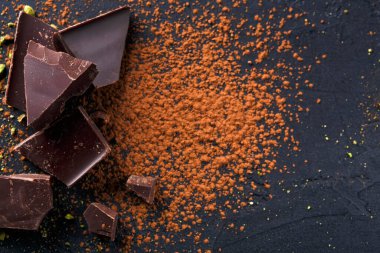 Çikolata parçaları, kakao tozu ve ezilmiş fındıkların yanında, koyu bir yüzeyde yatıyor. Ayarlar malzemelerin dokuları ve renkleri üzerinde bir odak gösterir.