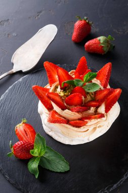 Taze çilek ve nane yapraklarıyla kaplı kremalı bir tatlı siyah bir taş tabağa yerleştirilir. Bütün çilekler tatlıya yerleştirildi..