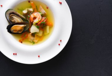 Beyaz bir kasede bir tabak deniz ürünleri çorbası servis edilir. Filmde karides, midye ve çeşitli sebzeler yer alıyor. Çorba berrak ve otlarla süslenmiş. Kırmızı biberler etrafa saçılmış..