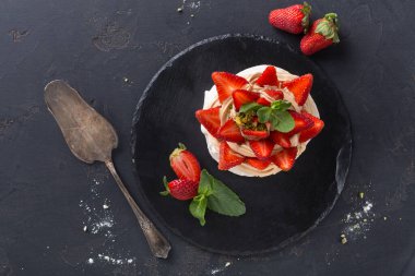 Tatlı, yanında gümüş servis spatulası olan siyah bir tabağa konur. Tatlı taze çilek ve nane ile kaplıdır. Başıboş çilekler tabakta..