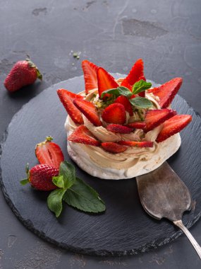 Üzerine taze çilek konmuş bir tatlı koyu bir levha yüzeyinde duruyor. Tabakta krem şanti ve nane var. Tatlının yanına bir kaşık konur..