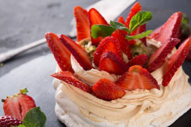 Krem şanti ile yapılan bir tatlı siyah bir tabakta taze çilekle süslenir. Sahne, tatlının parlak renklerini ve dokularını yakalar. Ayarlar sıradan bir yemek deneyimi gösteriyor..