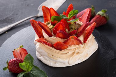 Yuvarlak bir tatlı siyah servis tahtasına oturur. Krema ve taze çilekle kaplanmış bir krema tabanı içeriyor. Nane yaprakları üzerine ve yakınına konur..