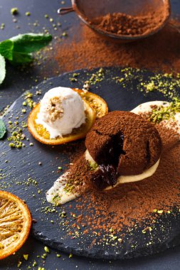 Bir tatlı erimiş çikolatayla dolu bir çikolatalı pasta içerir. Bir kepçe dondurma ve portakal dilimleriyle servis ediliyor. Tabak pudra kakao ve nane yapraklarıyla süslenmiş..