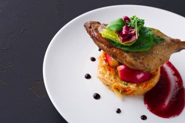 Tabakta sebze yatağında oturan bir parça tavuk var. Tabakta renkli süsler ve bir tutam sos yer alıyor. Çekici ve yemek için iyi hazırlanmış görünüyor..