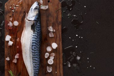Bütün bir balık ahşap bir kesme tahtasına yerleştirilir. Buz ve tuz etrafa saçıldı. Ayarlar, taze malzemelere odaklı mutfakta yemek pişirme hazırlığı öneriyor..