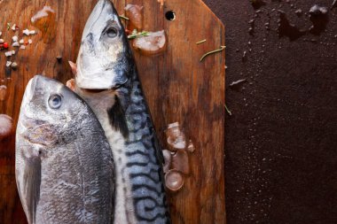 Mutfaktaki ahşap kesme tahtasına iki koca balık konur. Balıkların pulları var ve biraz da buz var. Bu sahne bir yemek hazırlığı öneriyor..