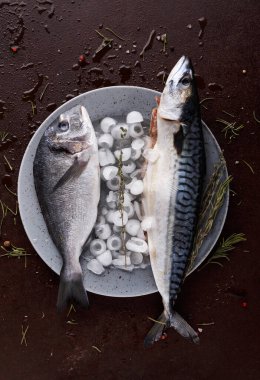 Buzla dolu bir tabakta iki tür balık dinleniyor. Mutfak tezgahı otlar ve etrafa saçılmış baharatlarla dolu. Bu sahne bir yemek hazırlığını yakalar..