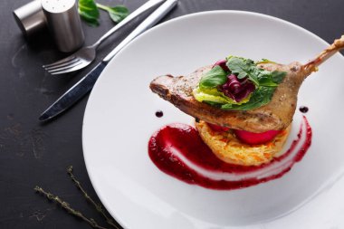 Bir tabak, marul ve soslu pirince konmuş otlarla kaplı bir ördek bacağı servis eder. Ayarlar yemek takımlarını ve bir yemek kurulumu için basit bir tasarımı gösteriyor.