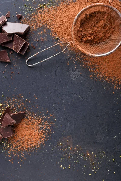 Kakao tozu, çikolata parçaları ve ince bir elek ile birlikte koyu bir yüzeye saçılmıştır. Sahne, mutfak ortamında pişirme ya da tatlı hazırlamayı öneriyor..