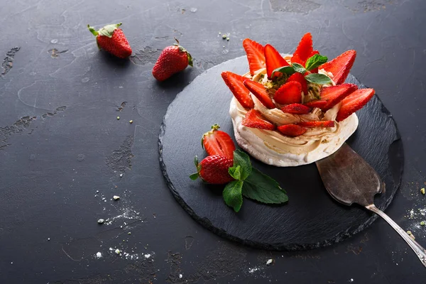 Koyu bir tahta yüzeyde bir tatlı düzenlenir. Sergide krema ve taze çilek ve nane yapraklarıyla süslenmiş bir taban yer alıyor. Çilekler yakınlarda..