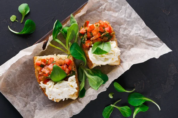 İki dilim ekmek domates karışımı ve peynirle kaplıdır. Tahta bir tahtanın üzerinde kahverengi bir kağıda yerleştiriliyorlar. Taze yeşiller, karanlık yüzeydeki dilimlerin etrafını sarar..
