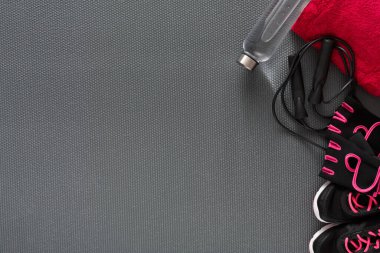 Yere bir yoga minderi konur. Yakınlarda bir su şişesi, bir havlu ve pembe bağcıklı siyah bir spor ayakkabı var. Kulaklıklar da görünür, alıştırma sırasında kullanılmaya hazırdır..