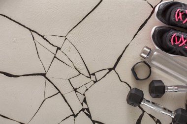 Dambıl ve su şişesi bir çift koşu ayakkabısının yanına yerleştirilir. Çatlak bir zeminde dinleniyorlar. Vites bir egzersiz alanında egzersiz oturumuna hazırlık gösteriyor.