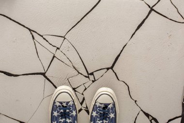 İçinde yıldız desenleri olan iki renkli ayakkabı çatlamış beyaz bir yüzey üzerinde duruyor. Çatlaklar yerde benzersiz bir desen oluşturuyor. Işık boşluğa girer, ayrıntıları vurgular.