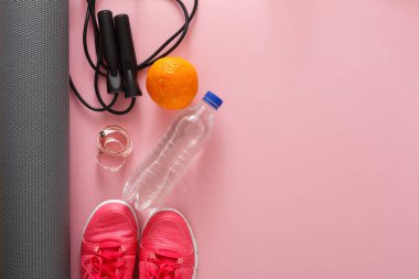 Pembe bir yüzeye bir dizi egzersiz malzemesi serilir. Spor ayakkabıları, su şişesi, atlama ipi, turuncu ve spor takip cihazı var. Bu ögeler antrenman için hazır..