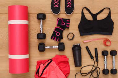 A workout space displays a yoga mat, dumbbells, a water bottle, fitness gloves, and clothing. The scene shows all items organized for a fitness session at home.
