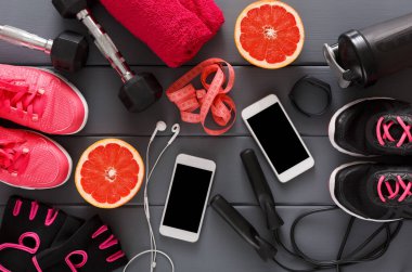 Parlak egzersiz ekipmanları ahşap bir yüzeye göre düzenlenir. Dambıllar, mezuralar, kulaklıklar ve iki akıllı telefon var. Taze greyfurt ve havlular olay yerine renk katar.