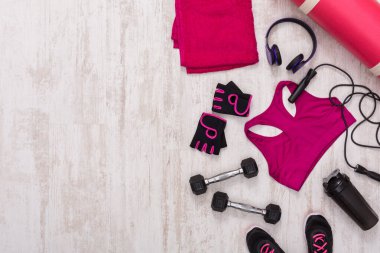 Bright colored towels and workout gear are arranged on a light wooden floor. The scene includes dumbbells, a water bottle, and headphones, ready for an exercise session.
