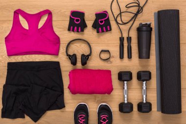Different items for a workout are laid out on a wooden floor. There are weights, resistance bands, a mat, and fitness clothing. It shows a plan to start an exercise routine at home.