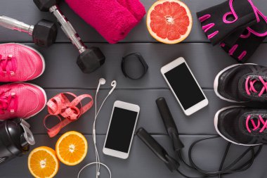 Various workout items are placed on a wooden surface. There are weights, exercise mats, fruit, and fitness gadgets. The scene shows preparation for an active and healthy session.