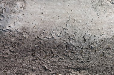 The wall shows a rough surface with cracks and uneven patches. The sun highlights the texture, creating contrast between light and shadow. Small details are visible in the walls design and wear.