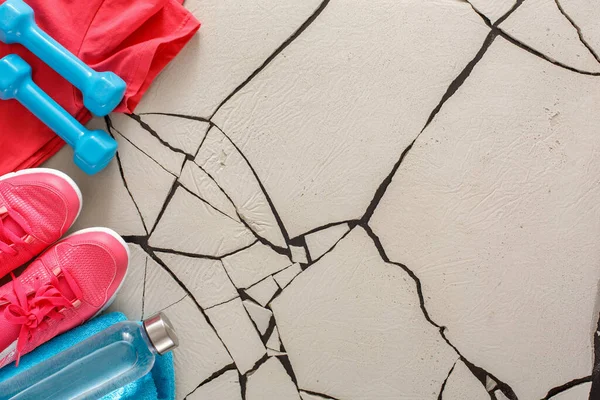 Parlak egzersiz ekipmanları çatlak bir katta ayarlandı. Pembe ayakkabılar, mavi bir havlu, bir dambıl ve bir su şişesi. Ayar bir egzersiz oturumuna hazır olduğunu gösterir.