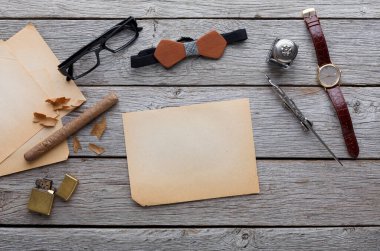 Çeşitli eşyalar ahşap bir masada düzenlenir. Eski kağıtlar, bir çift gözlük, bir saat, yazma aletleri ve birkaç dekoratif parça var. Bu sahne bir göreve hazırlanmayı öneriyor..