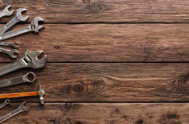 Çeşitli el aletleri ahşap bir masada düzenlenir. Anahtarlar, çekiç ve diğer aletler görünür. Bu ayar, tamirat ve projelerin yer aldığı bir atölye için tipik bir durumdur..