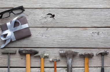 Çeşitli aletler, küçük bir hediye kutusunun yanındaki ahşap masada dizilmiş. Bu da bir projeye hazırlık olduğunu gösteriyor. Sahne, bir atölye ortamında iş ve kutlama karışımı öneriyor..