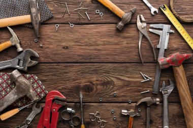 Aletler ve teçhizatlar ahşap bir masanın üzerine yayılmış. Anahtar, pense, vida ve çivi gibi şeyler. Sahne, çeşitli ekipmanları gösteren onarım veya DIY projeleri için bir çalışma alanını ortaya çıkarıyor.