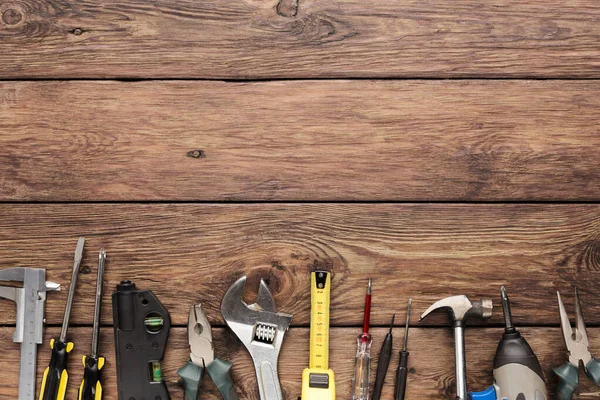 Ahşap bir yüzeyde çeşitli aletlerin bir koleksiyonu düzenlenir. Bu aletler arasında tornavida, pense, mezura ve daha fazlası var. Ev projeleri ve onarım için hazırlar..