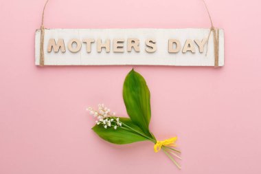 Anneler Günü için bir işaret küçük bir buket çiçeğin üzerinde asılı duruyor. Arka plan pembe ve çiçekler sarı bir kurdeleyle bağlanmış. Bu sahne şenlikli bir olayı yansıtıyor..