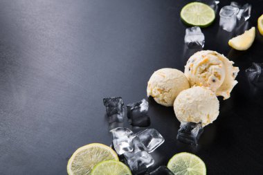 Limon dilimleri ve buzlarla birlikte üç kepçe dondurma düzenleniyor. Sahne karanlık bir yüzeye kurulmuş, soğuk ve ferahlatıcı malzemelerin altını çiziyor. Bu düzenek bir yaz ziyafeti öneriyor..