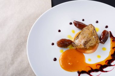 Bir şef, rengarenk soslar ve meyvelerle hazırlanmış pişmiş et içeren bir yemek sunar. Mekan, tabaktaki detaylara dikkat eden bir restoran..