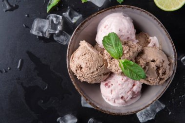 Bir kase dolusu çikolata ve çilekli dondurma içerir. Taze nane yaprakları ve limon dilimleri kasenin etrafına konur. Buz küpleri karanlık yüzeye dağılmış..