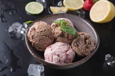 Farklı kepçe dondurmalar bir kasenin içinde buz küpleri, limon ve limon dilimleri ile çevrili. Ayrıca yanında taze çilekler de var. Tatlılar hazır..