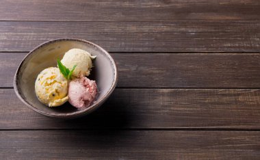 Bir kase üç kepçe dondurmayı farklı tatlarda, ahşap bir masanın üzerine koyar. Ayarlar üzerinde taze bir nane yaprağı olan basit bir düzenleme gösteriyor..