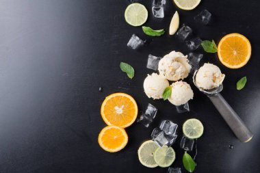 Dondurma parçaları karanlık bir yüzeye yerleştirilir. Dondurmanın etrafı portakal dilimleri, limon dilimleri ve nane yapraklarıyla çevrili. Meyvelerin etrafına dağılmış buz küpleri var..