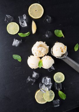 Limon ve limon dilimlerinin yanında metal bir kepçenin üzerinde bir kepçe limonlu dondurma. Olay yerini çevreleyen taze nane yaprakları ve buz küpleri siyah bir yüzey üzerinde ferahlatıcı bir yaz ziyafeti gösteriyor..