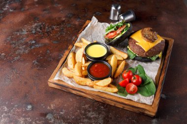 Tahta tepside peynirli, marullu ve mantarlı bir hamburger var. Hamburgerin yanında kızarmış patates ve iki kase sos var. Kiraz domatesleri ve taze yeşiller yemeği tamamlar..