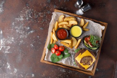 Yiyecek, içinde peynir, kızarmış patates, iki sos ve taze sebzeler bulunan ahşap bir tepside servis edilir. Yemek sıradan bir yemek bağlamında sunuluyor..