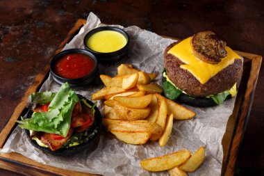 Bir tabakta peynirli bir hamburger ve yanında da kızarmış patates var. İki sos ve sebze ve domatesli bir salata var. Bu yemek sıradan bir lokantada servis edilir..