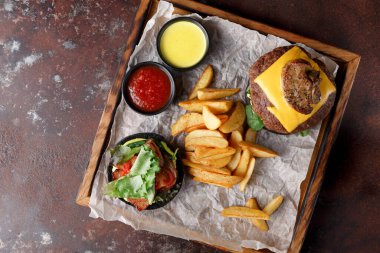 Peynirle kaplı lezzetli bir hamburger kızarmış patates ve ahşap tepside salatanın yanında oturur. İki küçük kase sos yemeği tamamlar. Bu birçok restoranda popüler bir seçenektir..