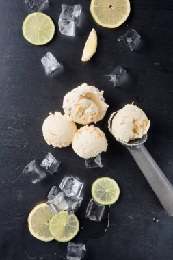 Limonlu dondurma kepçeleri buz küpleri ve limon dilimleriyle çevrili karanlık bir yüzeye yerleştirilir. Bu düzenek yaz boyunca ferahlatıcı bir ikram öneriyor. Parlak limon tadı soğuk buzu tamamlıyor..