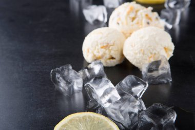 Üç kepçe dondurma karanlık bir masaya konur. Dondurmanın etrafında dondurma ve taze limon dilimleri var. Sahne, sıcak bir günde ferahlatıcı bir ikram sunar..